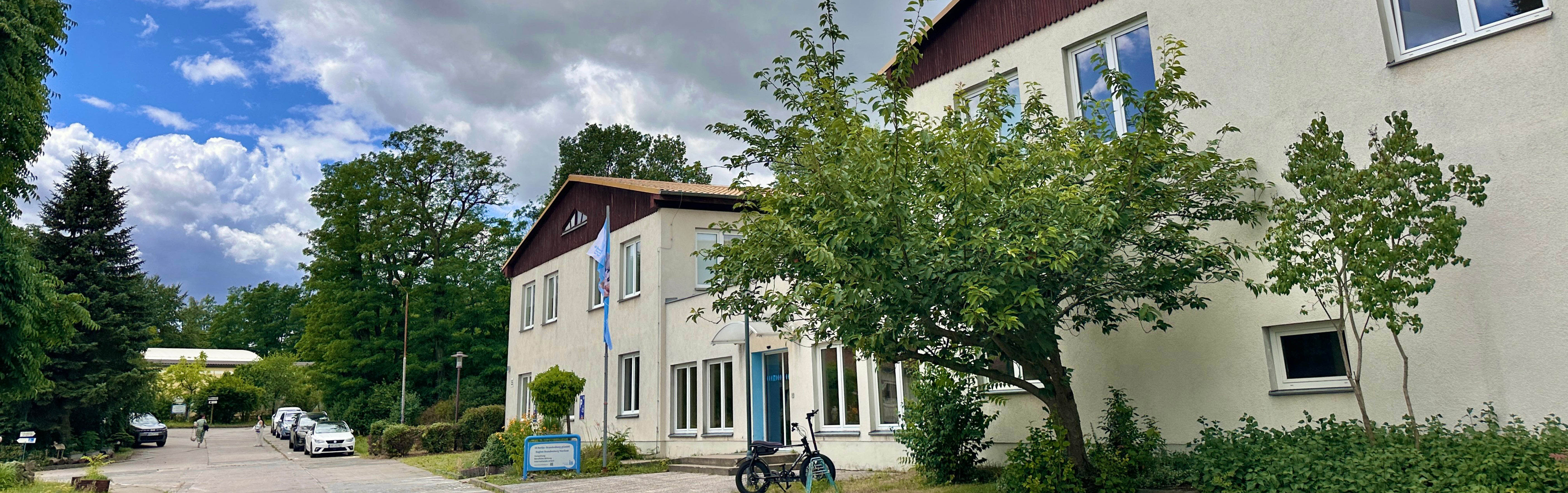 Außenansicht eines modernen Bildungs- und Verwaltungsgebäudes in Frankfurt (Oder) mit begrüntem Außengelände, Zufahrt, Fahrradstellplatz und bewölktem Himmel.