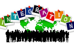 Eine Gruppe von Silhouetten vor einer Weltkarte, darüber bunte Buchstaben, die das Wort „Integration“ bilden.